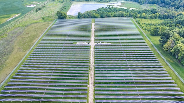 An aerial view of a large solar farm with rows of solar panels stretching across a rural landscape, under a clear blue sky. The image illustrates the scale and impact of renewable energy projects on the environment.