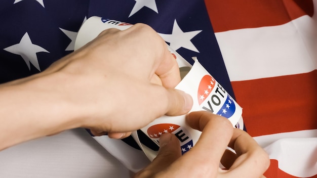 Close-up of a hand placing a ballot into a ballot box. The ballot has an 