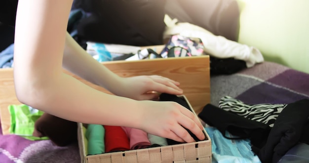 A close-up of a hand sorting through clothing in a closet, separating items to keep, donate, and discard, with organized shelves and drawers visible in the background.
