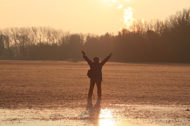 A person standing outside in the early morning sunlight, arms outstretched, feeling the warmth, with trees and a clear sky in the background, conveying a sense of connection with nature and energized well-being.