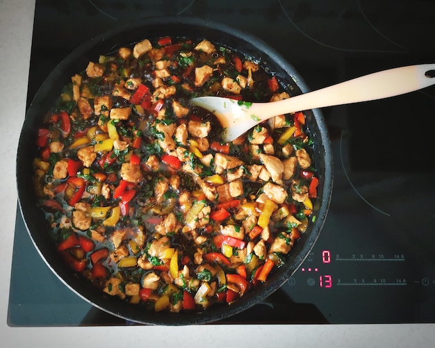 Top-down shot of a person preparing a batch of chicken and veggie stir-fry in a wok, showcasing the colorful vegetables and evenly cooked chicken pieces.