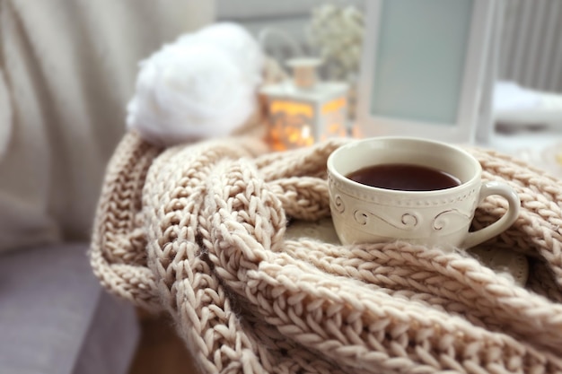 A close-up of a knitted blanket with a textured pattern, draped over a chair, with a mug of steaming tea and soft, warm lighting.