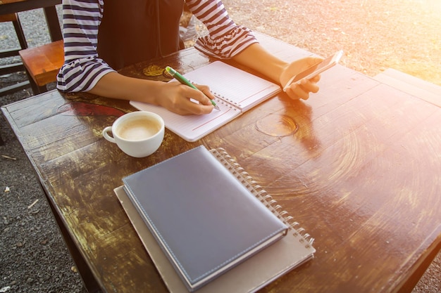 A person's hands holding a journal and a pen, resting on a wooden table. Sunlight streams through a window, illuminating the scene. The background is blurred, creating a sense of tranquility and focus on the act of journaling.