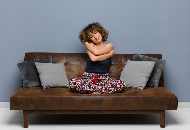 A person sitting comfortably on a couch with a blanket, surrounded by pillows, and engrossed in watching a TV series on a large screen. The room is dimly lit, creating a cozy and inviting atmosphere for binge-watching.